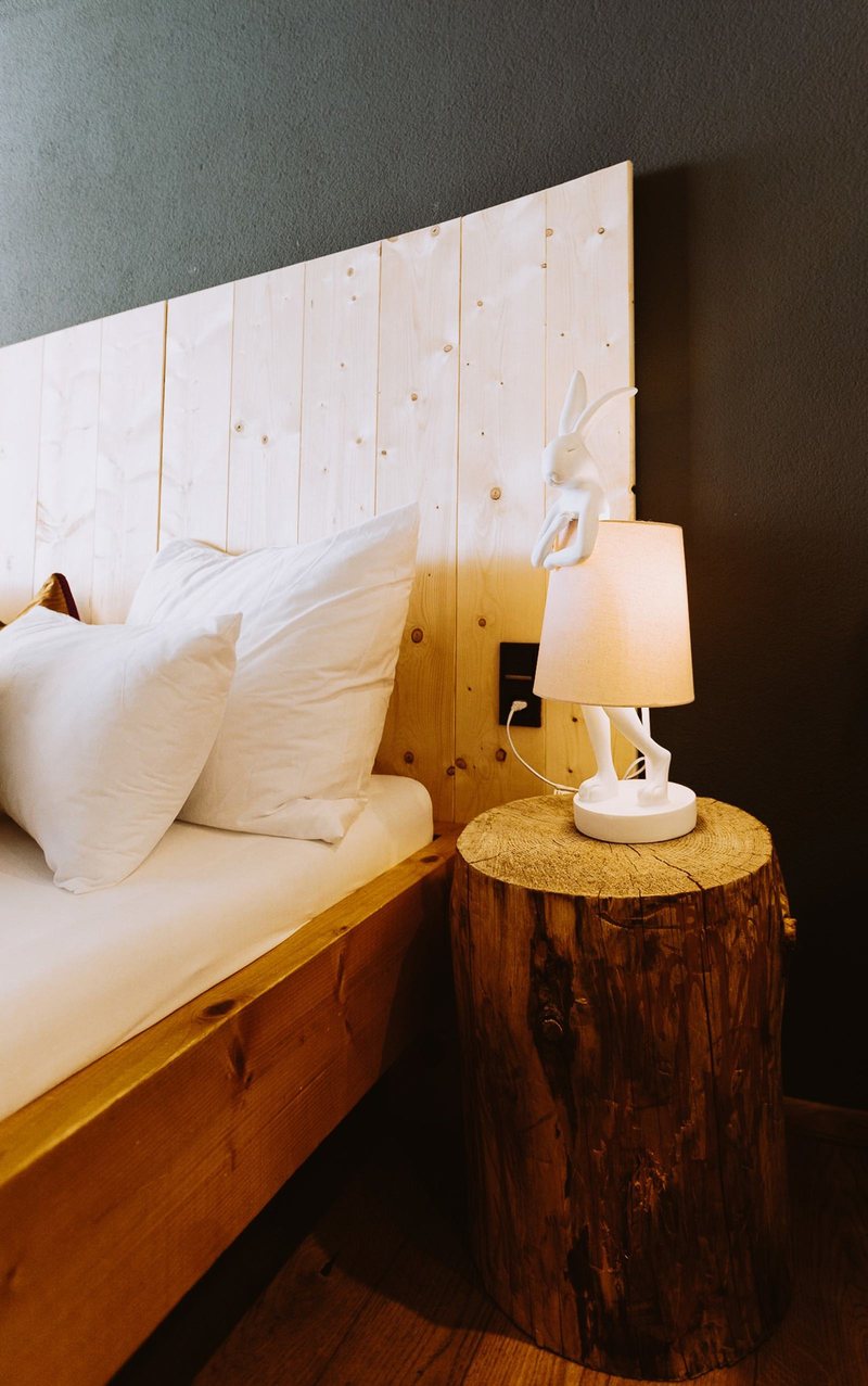 Bettecke mit Nachttisch aus Baumstamm und Lampe in einem Zimmer im Walliserhof