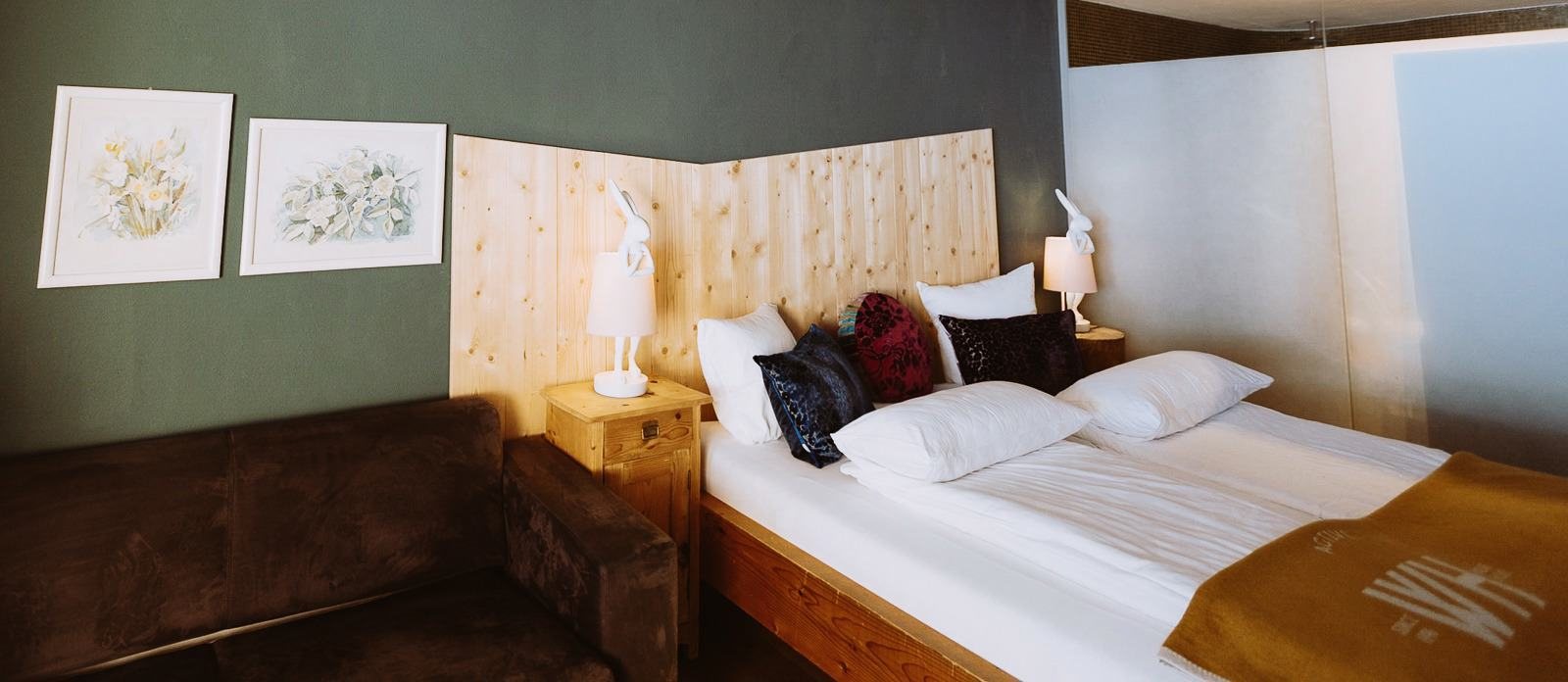Doppelbett und Sitzbank vor grüner Wand in einem Alpinista-Zimmer im Walliserhof