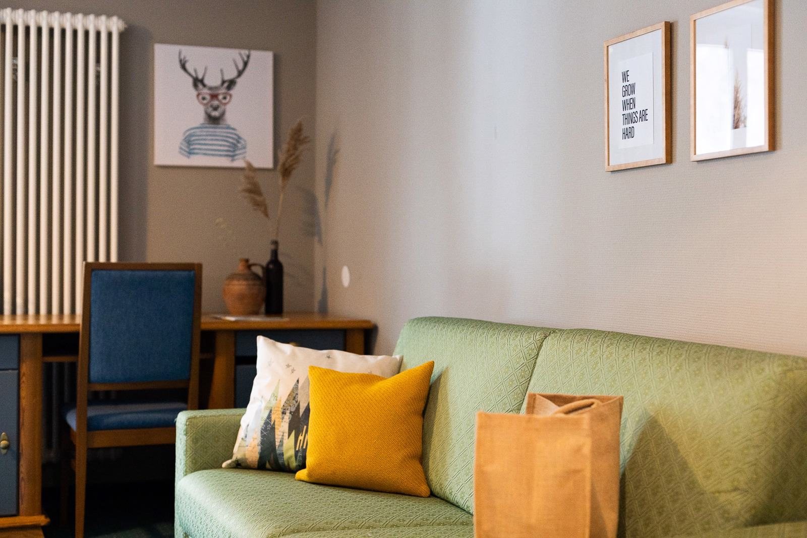 Grünes Sofa mit gelbem Kissen und Hirschbild in einem Scesa-Zimmer