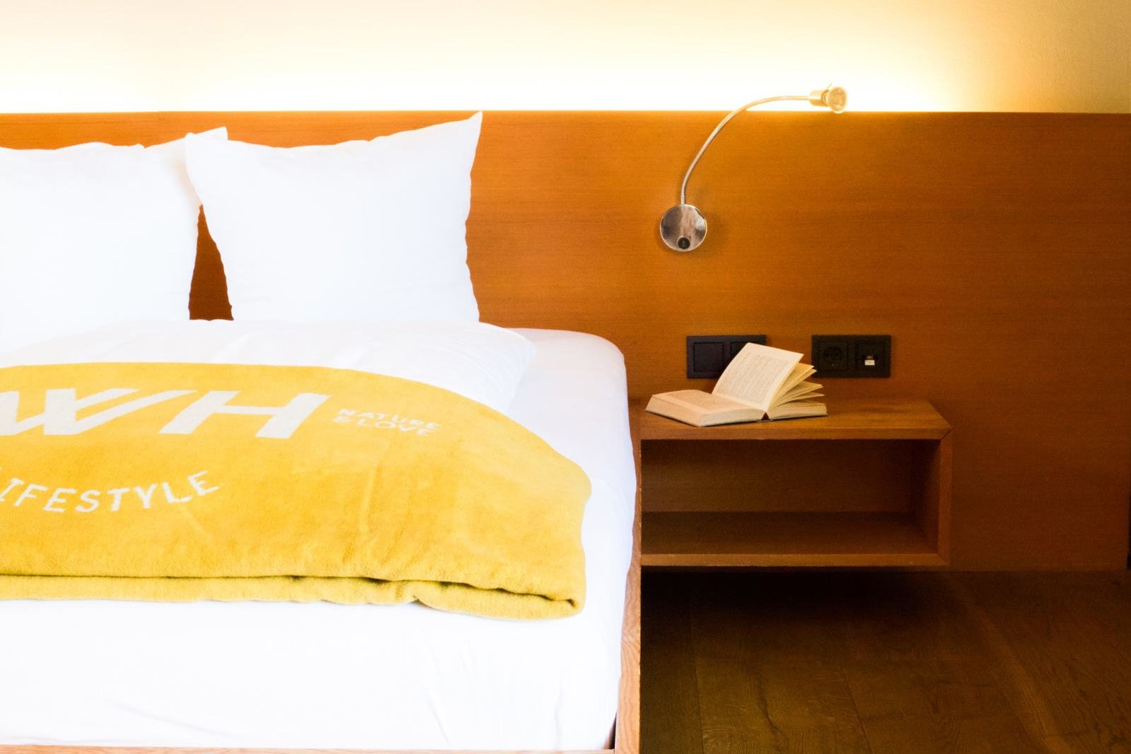Bett mit gelber Walliserhof-Decke und Leselampe in einer Suite