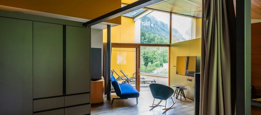 Moderne Hotelzimmer mit gelben Wänden, einem großen Fenster, einem blauen Stuhl und Holzakzenten.
