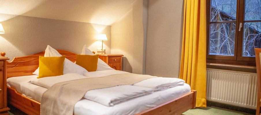 Gemütliches Schlafzimmer mit einem Holzbett, gelben Vorhängen und warmem Licht.