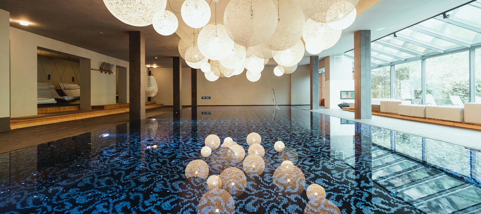 Innenpoolbereich mit blauen Mosaikfliesen und großen, dekorativen Pendelleuchten darüber.