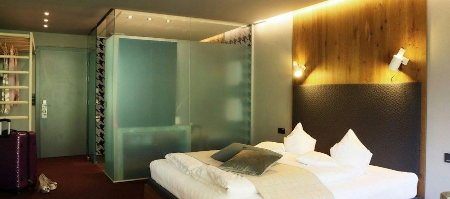 Modernes Hotelzimmer mit einem Bett, Glaspartition, Gepäck und stilvollen Holzakzenten.