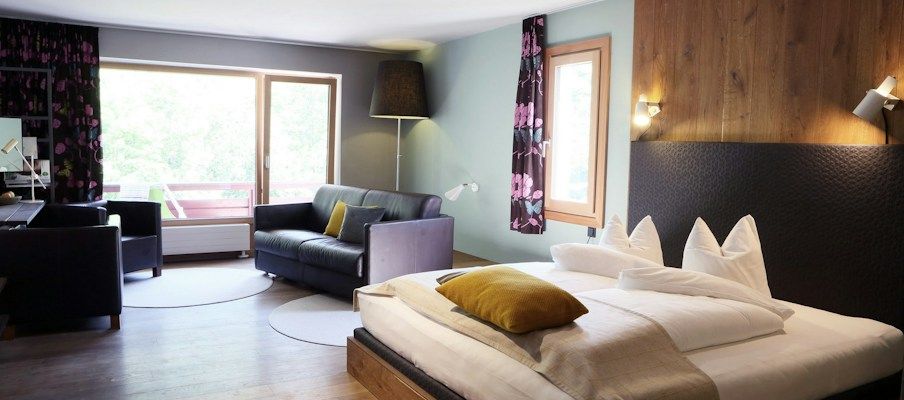 Ein modernes Hotelzimmer mit einem Doppelbett, Sofa und großem Fenster mit natürlichem Licht.