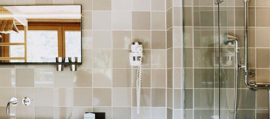 Modernes Badezimmer mit gefliesten Wänden, einem großen Spiegel und einer Glast Dusche.
