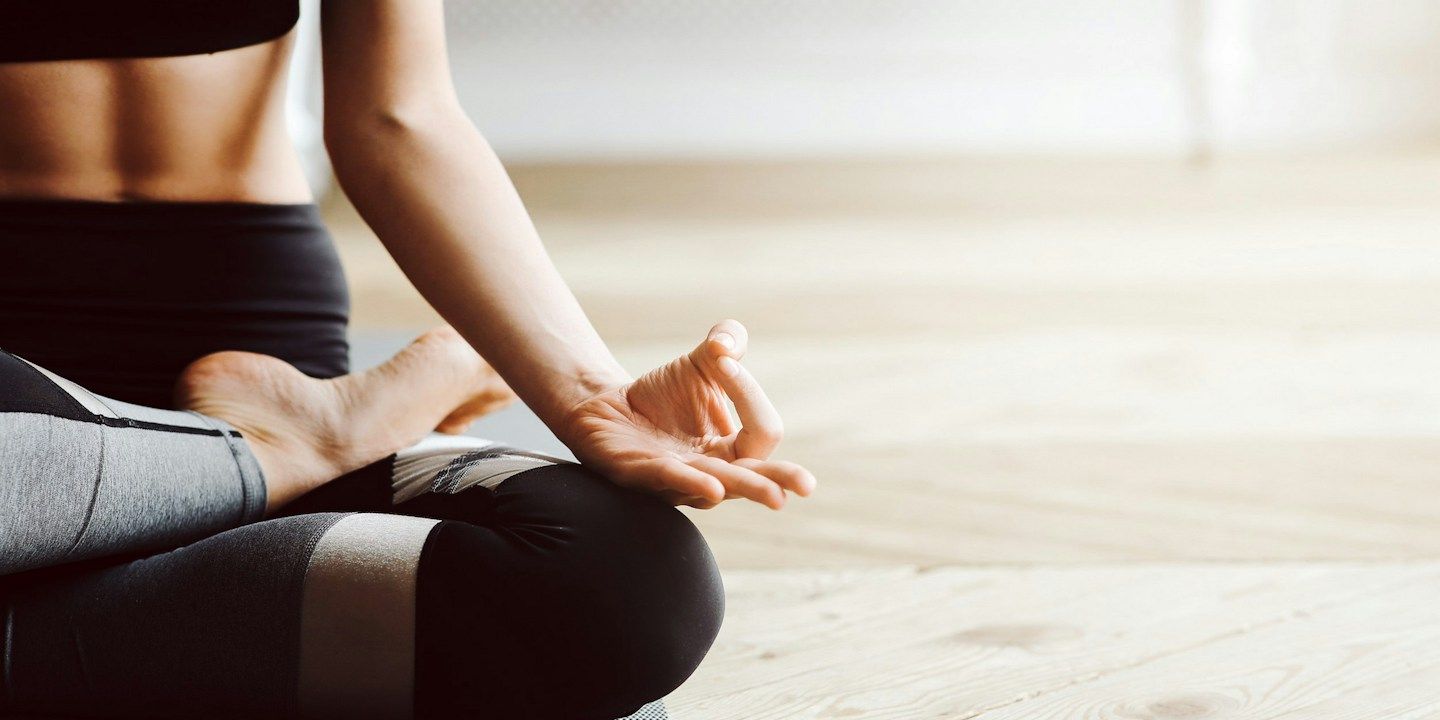 Eine Person in Yoga-Kleidung, die im Schneidersitz meditiert und eine Handgeste macht.