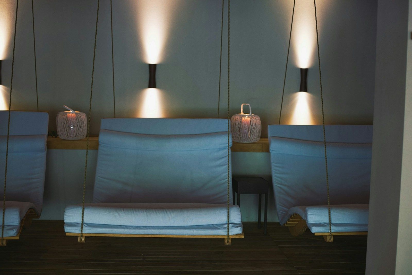 Zwei hängende Liegen mit blauen Kissen, beleuchtet von warmem Licht und seitlichen Laternen.