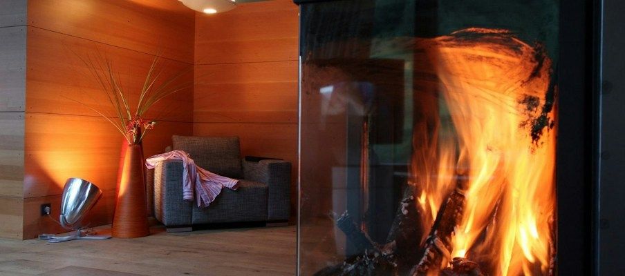 Gemütliches Wohnzimmer mit modernem Kamin, einem grauen Sessel und dekorativen Pflanzen bei warmem Licht.