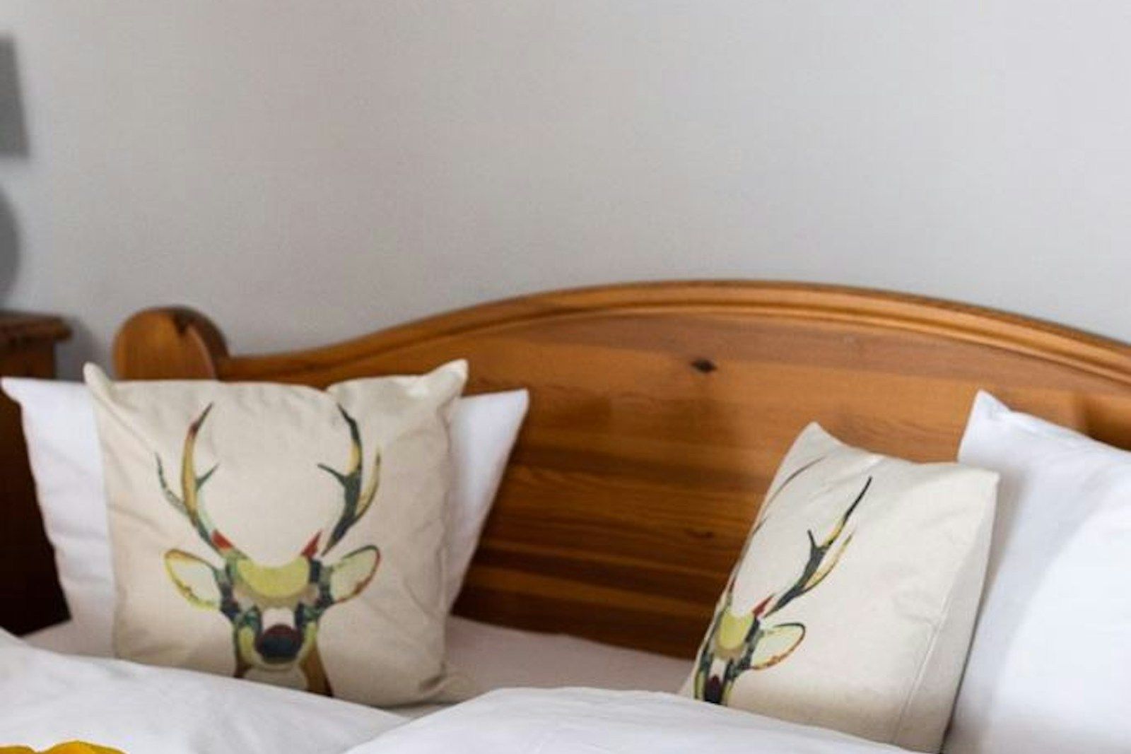 Ein gemütliches Bett mit weißen Bettwaren, gelbem Überwurf und Dekorkissen mit Hirschgeweihen.