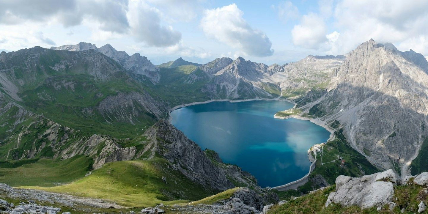 Panoramablick auf Berge, die einen blauen See unter einem teilweise bewölkten Himmel umgeben.