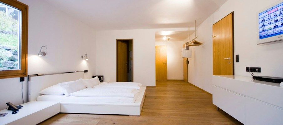 Modernes Hotelzimmer mit einem Bett, Holzboden und einem wandmontierten Fernseher.